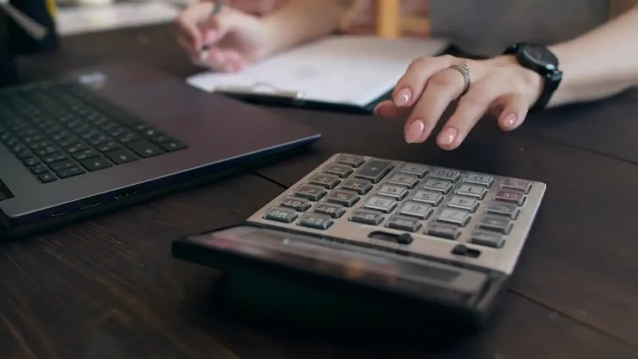 Accountant working through figures on a calculator beside a laptop and printed records