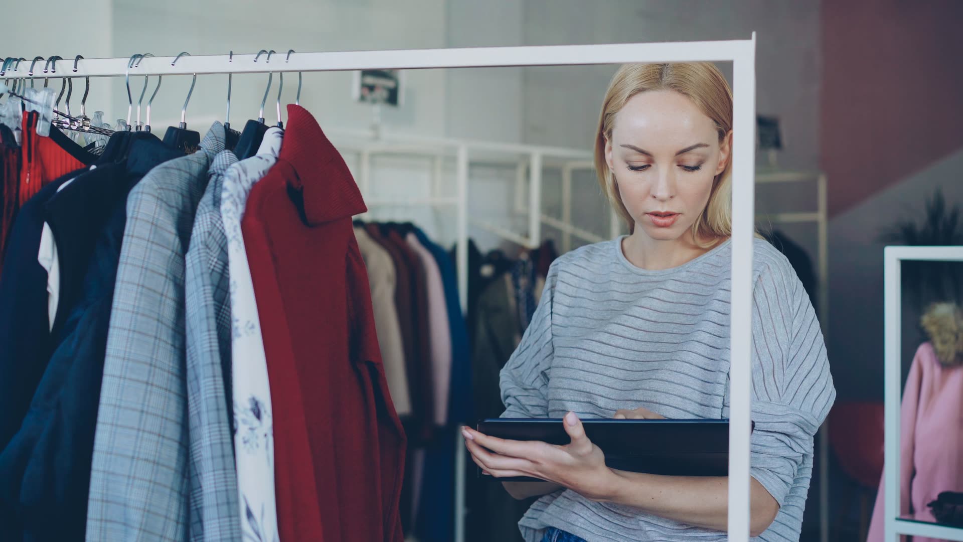 Retail employee reviewing store inventory on a tablet beside clothing rails