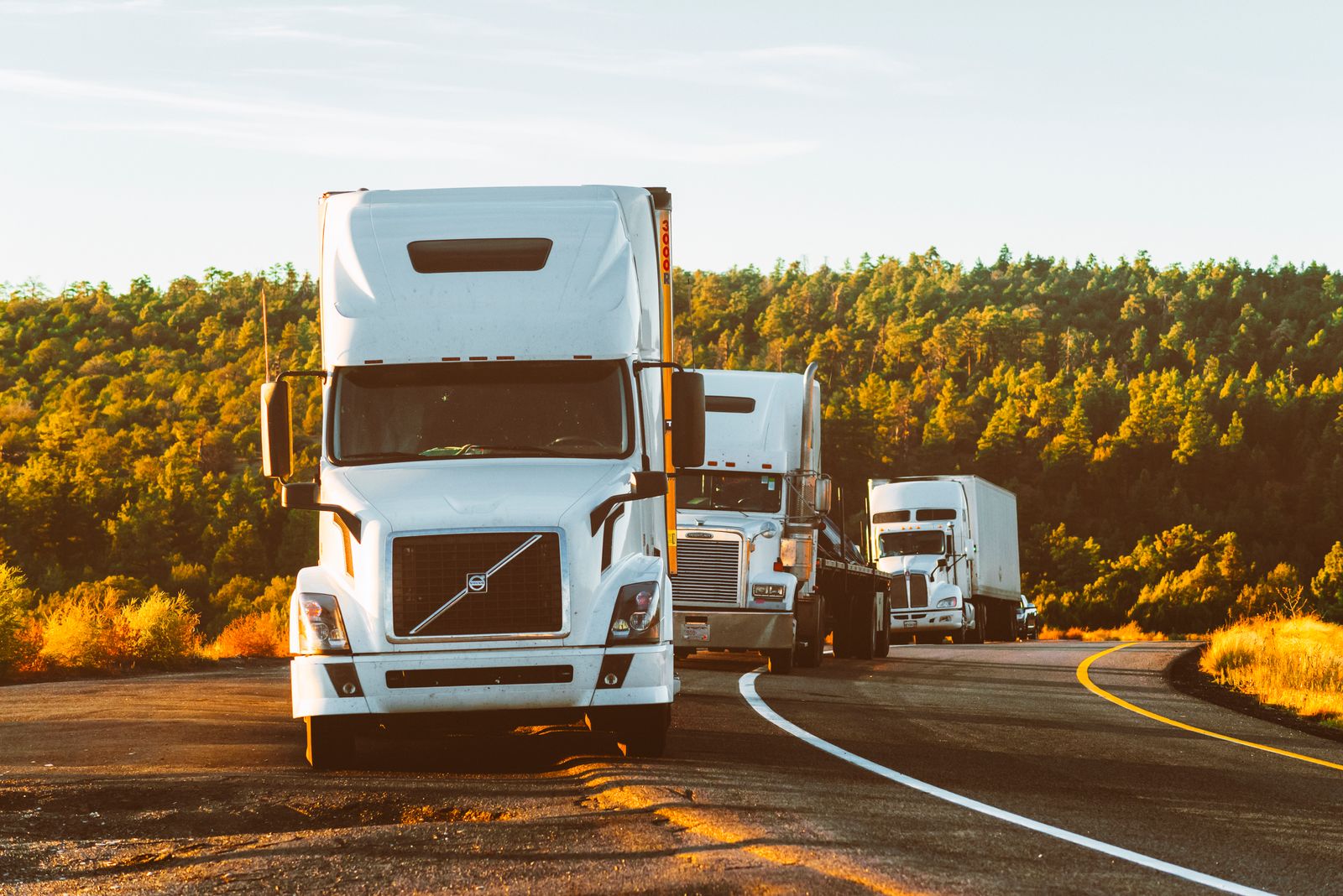 White commercial trucks parked along a highway during golden hour